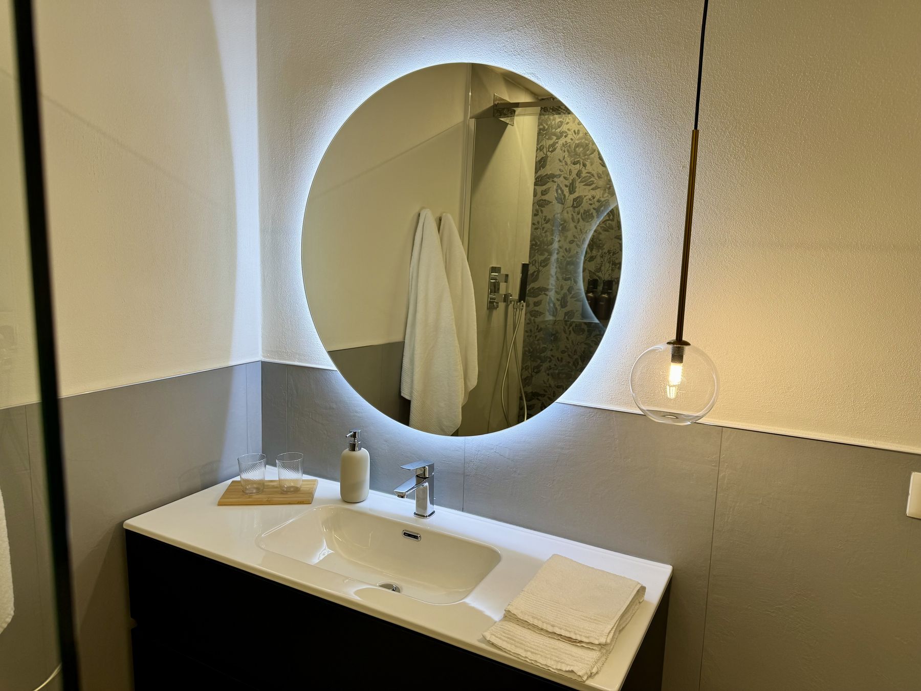 Il lavabo sospeso con specchio tondo retroilluminato nel bagno della Camera Aria