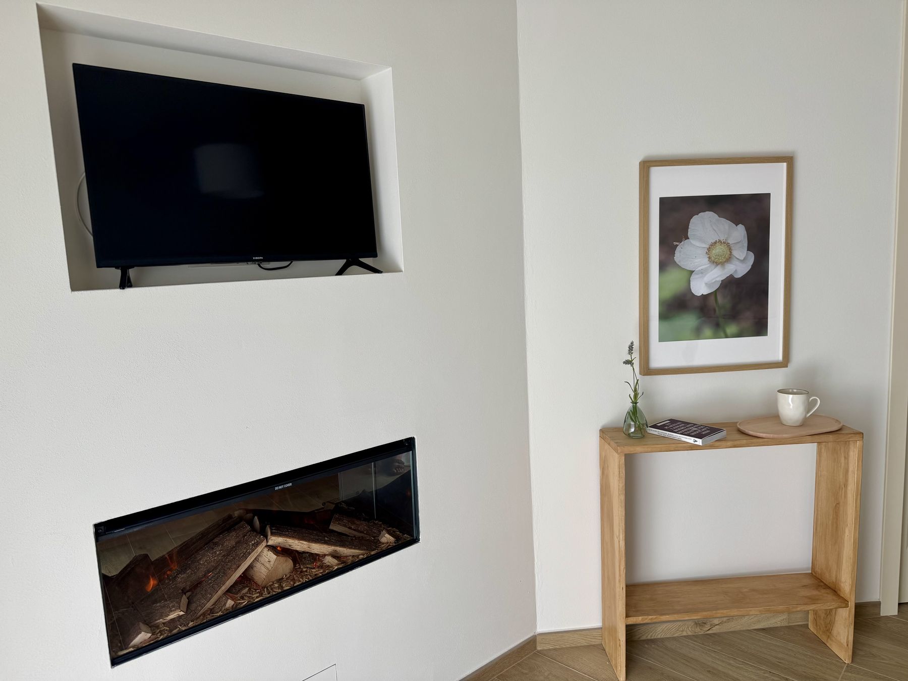 Il camino elettrico a parete, la smart TV in nicchia e la consolle in legno della Camera Giardino