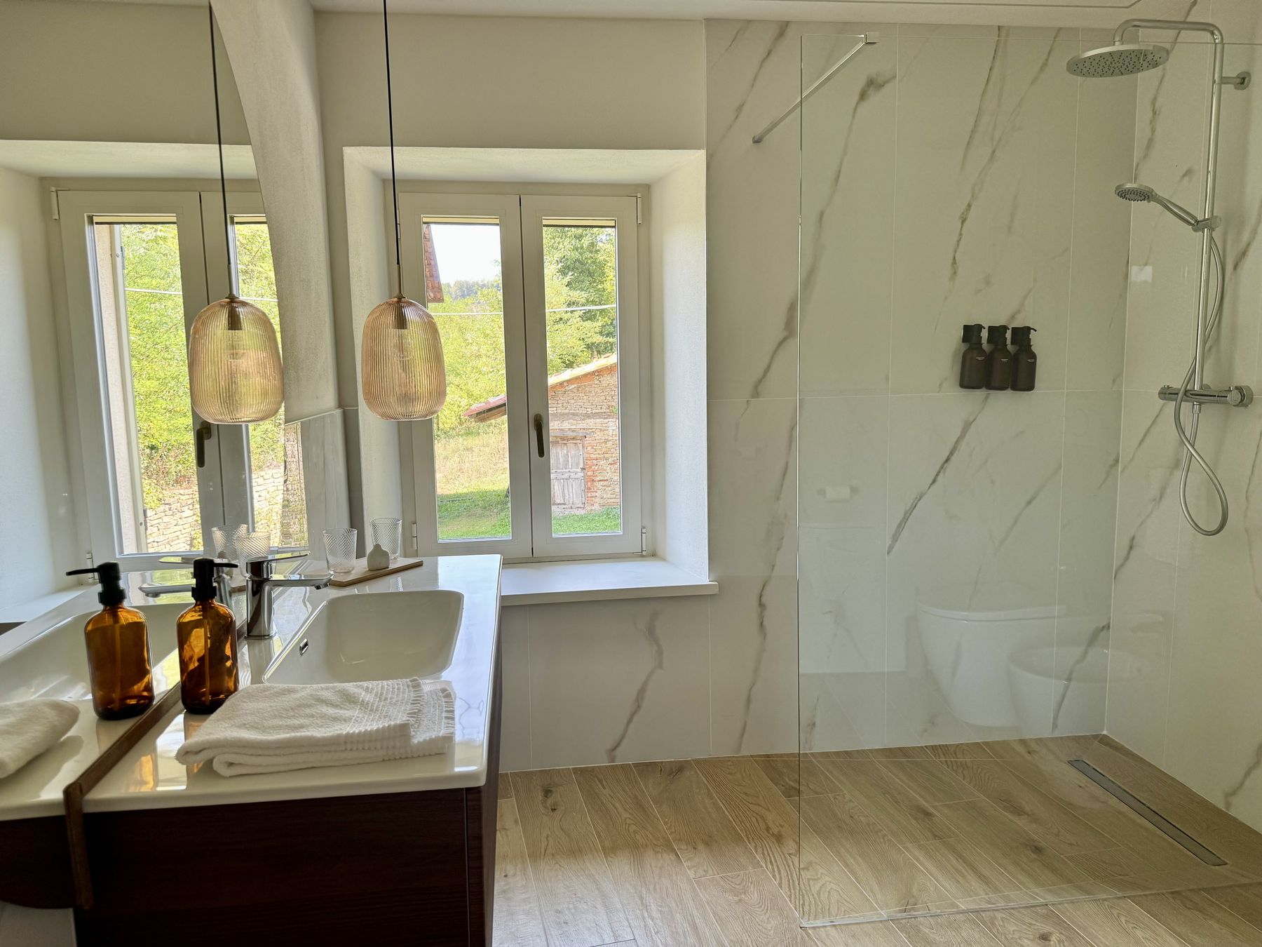 Il grande bagno della Camera Giardino con doccia walk-in in marmo chiaro e due finestre sul verde