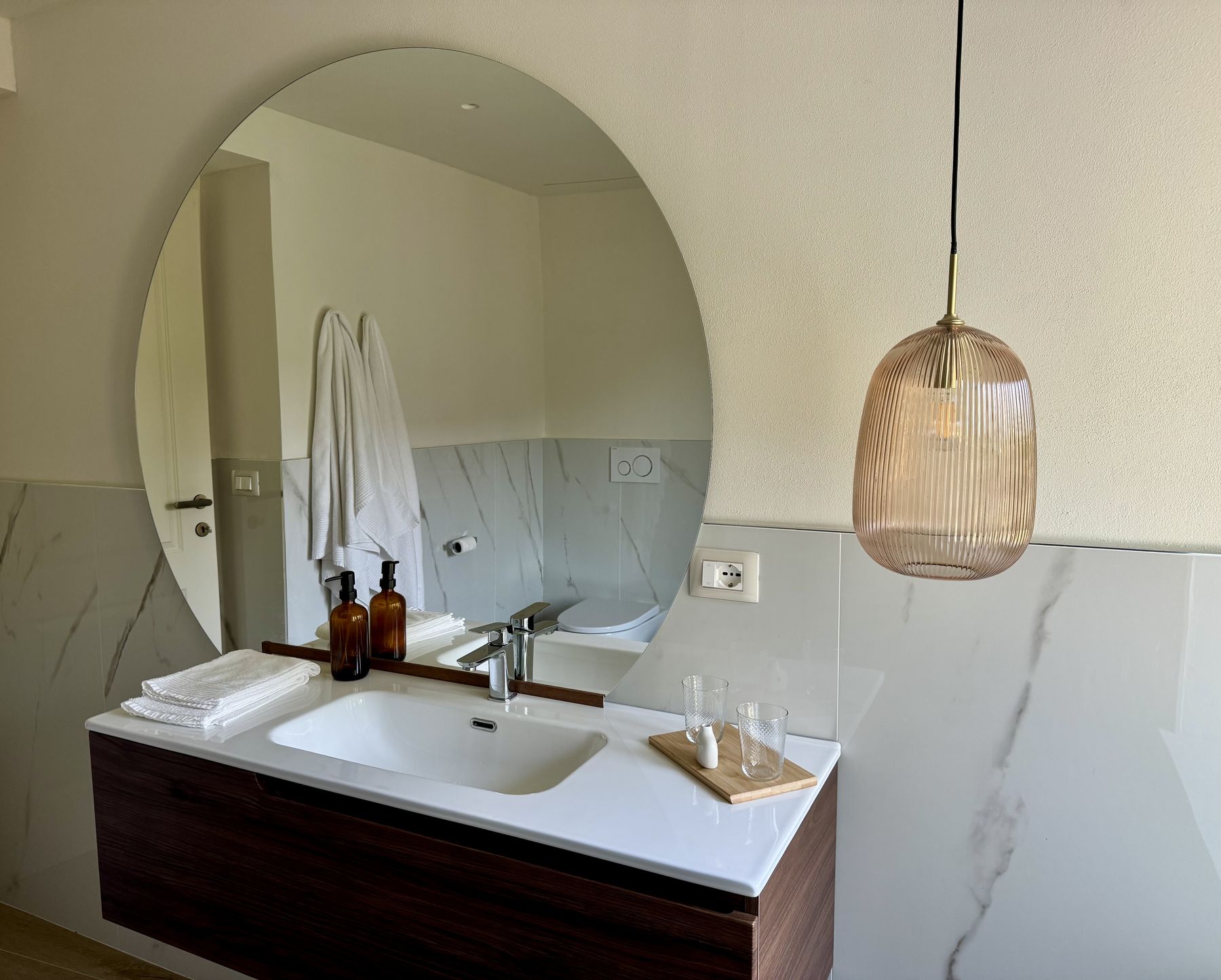 Il lavabo con specchio tondo e lampada in vetro ambrato nel bagno della Camera Giardino
