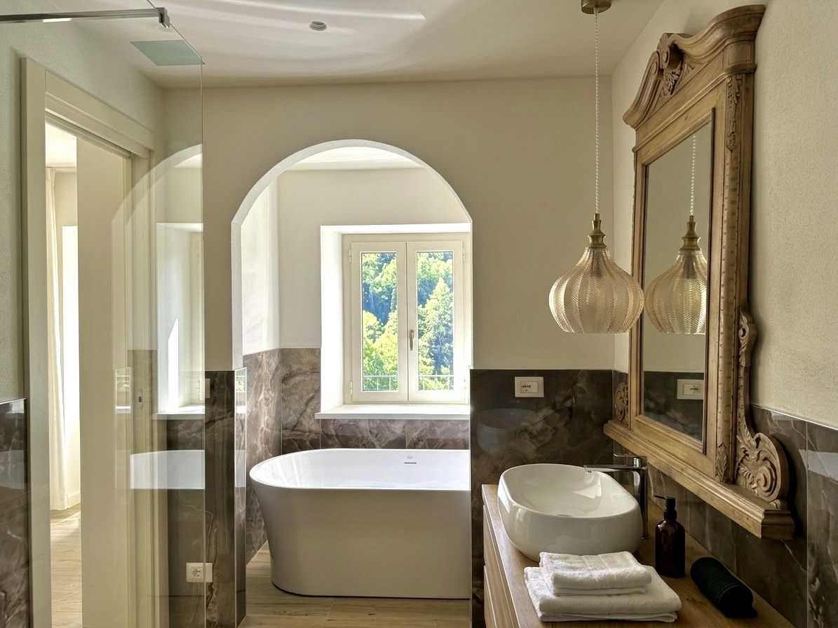 La vasca freestanding sotto l'arco e il lavabo d'appoggio con specchiera dorata nel bagno della Camera Terra