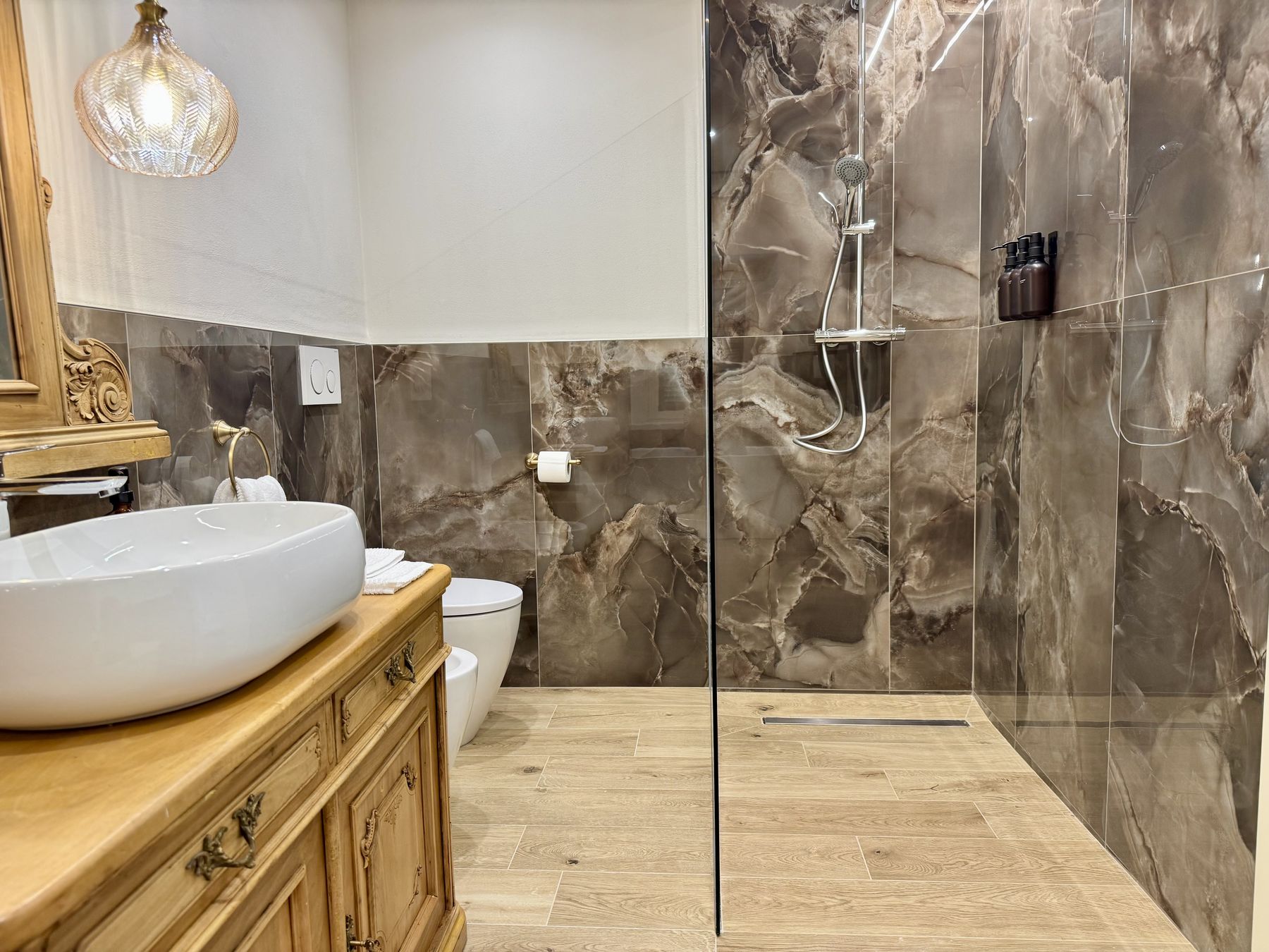 La doccia walk-in con lastre effetto marmo scuro e il mobile lavabo antico della Camera Terra
